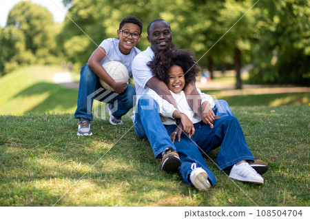 Dad and two kids sitting on the grass in the park 108504704
