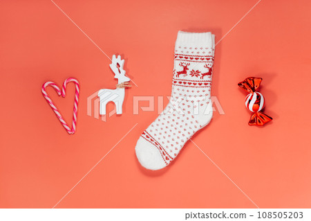 Minimalist Christmas mood concept. Red Background with Christmas attributes as candy canes in the shape of heart, warm socks, wooden deer decoration and candy toy. Flat lay, top view. Copy space. Minimalist Christmas mood concept. Red Background with Christmas attributes as candy canes in the shape of heart, warm socks, wooden deer decoration and candy toy. Flat lay, top view. Copy space. 108505203