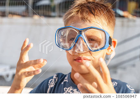 Boy puts on diving mask on beach at gentle sunset light Boy puts on diving mask on beach at gentle sunset light 108506947