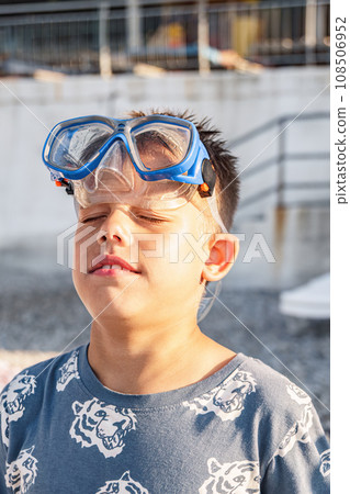 Handsome smiling boy with diving mask on head rests on beach Handsome smiling boy with diving mask on head rests on beach 108506952