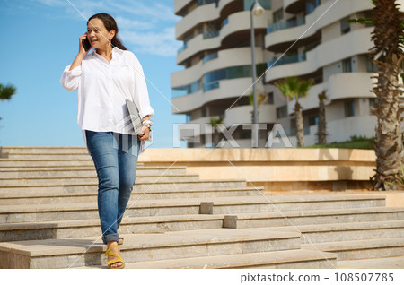 Female entrepreneur, office worker going to the work, talking on mobile phone, holding laptop, thoughtfully looking away Female entrepreneur, office worker going to the work, talking on mobile phone, holding laptop, thoughtfully looking away 108507785