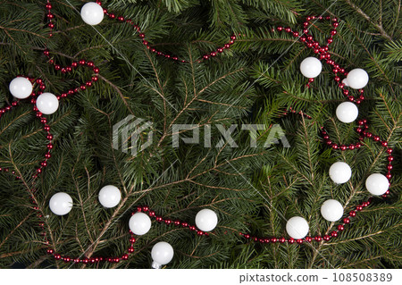 zoom on a pile of fir branches with a frame of bright red pearl garland and many christmas bauble 108508389