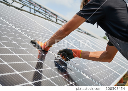 Close up of man hands in work gloves mounting photovoltaic solar panels. Male worker assembling solar modules for generating electricity through photovoltaic effect. Renewable energy sources concept. Close up of man hands in work gloves mounting photovoltaic solar panels. Male worker assembling solar modules for generating electricity through photovoltaic effect. Renewable energy sources concept. 108508454