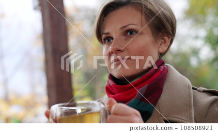 Positive businesswoman enjoys hot drink sitting in gazebo overlooking countryside. Businesswoman rest and break for hot drink. Enjoying hot drink and relaxed businesswoman in country house yard Positive businesswoman enjoys hot drink sitting in gazebo overlooking countryside. Businesswoman rest and break for hot drink. Enjoying hot drink and relaxed businesswoman in country house yard 108508921