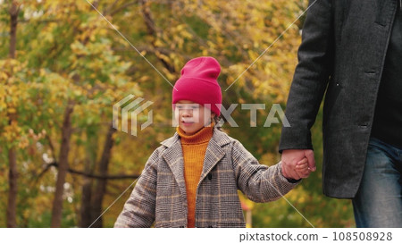 Playful little girl with father walk holding hands in warm autumn park. Happy little daughter and father enjoy walking in fall park. Father and little daughter rest in garden on autumn weekend Playful little girl with father walk holding hands in warm autumn park. Happy little daughter and father enjoy walking in fall park. Father and little daughter rest in garden on autumn weekend 108508928