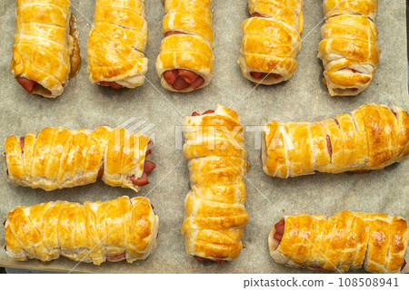 Close-up of baked sausages in dough on baking paper. 108508941