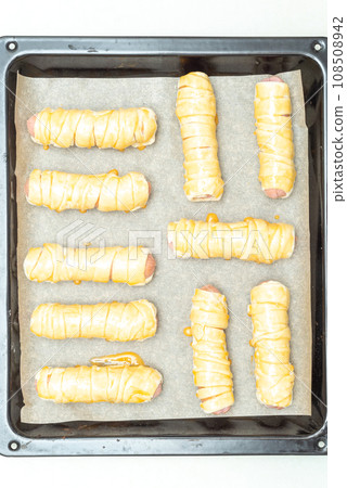 Top view of a baking sheet with sausages in raw dough greased with egg yolk. 108508942
