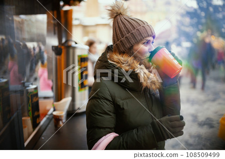 woman in green coat and brown hat at christmas fair in city 108509499