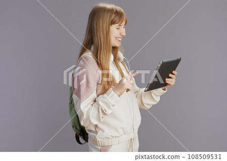 smiling modern school girl in beige tracksuit using tablet PC 108509531