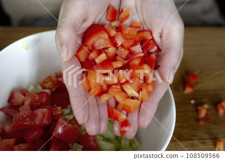 A woman's hands sprinkles small pieces of paprika close-up. Prepare salad as a side dish for the main dish. High quality photo. 108509566