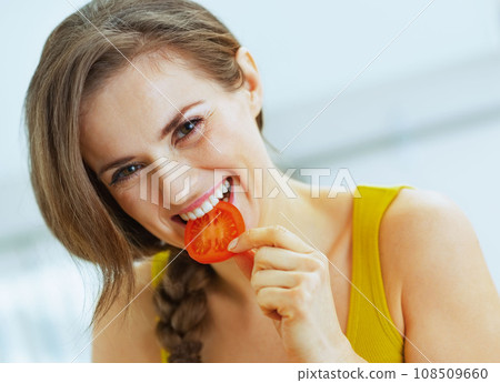 Happy young woman having bite of red tomato 108509660