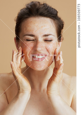 smiling young woman with face scrub isolated on beige 108509773