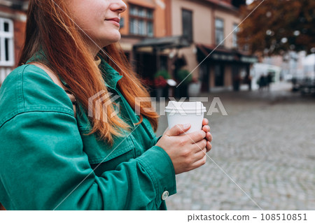 Woman is holding paper coffee cup or tea on urban background. Take away or delivery concept. Copy space. Autumn lifestyle. Place for your text on mug, mockup. 108510851
