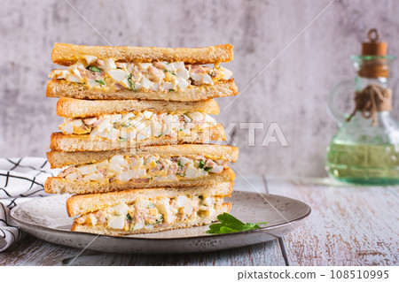 Stack of chopped egg, bacon and herb salad sandwiches on a plate 108510995
