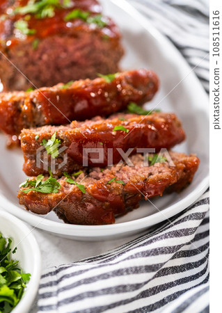 Slicing classic meatloaf with a sweet glaze on a white serving plate Slicing classic meatloaf with a sweet glaze on a white serving plate 108511616