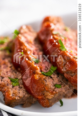 Slicing classic meatloaf with a sweet glaze on a white serving plate 108511619