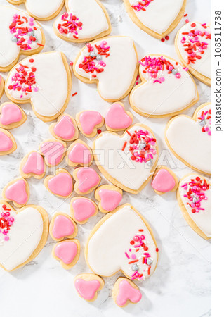 Decorating heart-shaped sugar cookies with pink and white royal icing for Valentine's Day. 108511738