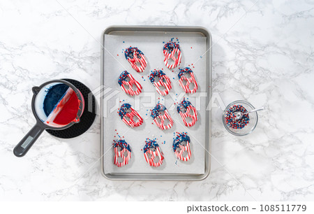 Flat lay. Dipping pretzels twists into melted chocolate to make red, white, and blue chocolate-covered pretzel twists. Flat lay. Dipping pretzels twists into melted chocolate to make red, white, and blue chocolate-covered pretzel twists. 108511779