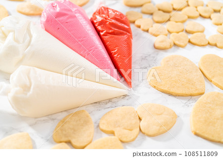 Decorating heart-shaped sugar cookies with pink and white royal icing for Valentine's Day. Decorating heart-shaped sugar cookies with pink and white royal icing for Valentine's Day. 108511809