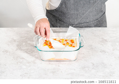 Pouring fudge mixture into the square glass baking pan lined with parchment paper to prepare candy corn fudge. Pouring fudge mixture into the square glass baking pan lined with parchment paper to prepare candy corn fudge. 108511811