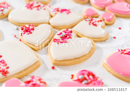 Decorating heart-shaped sugar cookies with pink and white royal icing for Valentine's Day. Decorating heart-shaped sugar cookies with pink and white royal icing for Valentine's Day. 108511817