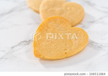 Decorating heart-shaped sugar cookies with pink and white royal icing for Valentine's Day. Decorating heart-shaped sugar cookies with pink and white royal icing for Valentine's Day. 108511864