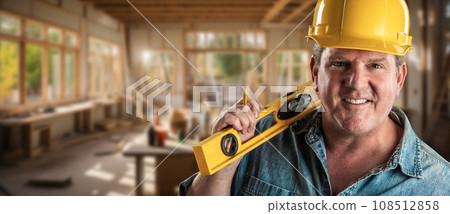 Hard Working Male Contractor at a Construction Site Wearing a Hard Hat and Work Gloves Holding His Level. Hard Working Male Contractor at a Construction Site Wearing a Hard Hat and Work Gloves Holding His Level. 108512858