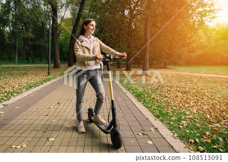 Young beautiful stylish woman riding electric scooter by autumn park, ecological transport Young beautiful stylish woman riding electric scooter by autumn park, ecological transport 108513091