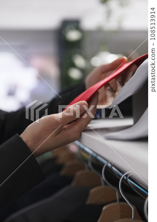 Department center clothing store seller hands adjusting red tie while organizing accessory on display shelf closeup. Fashion boutique seller arms holding merchandise, checking garment stock Department center clothing store seller hands adjusting red tie while organizing accessory on display shelf closeup. Fashion boutique seller arms holding merchandise, checking garment stock 108513914