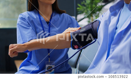 Assistant doing hypertension examination with tonometer in hospital waiting room, measuring asian patient blood and pulse pressure. Cardiologist nurse checking hypotension with cardiology instrument. 108513922