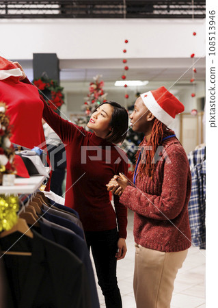 Employee presenting clothes to customer, asian woman looking for fashion items to give as christmas presents in retail store. to Shopping manager recommending accessories for dinner preparations. 108513946
