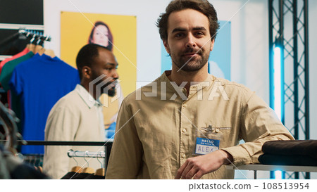 Shopping center assistant posing in clothing store, man working in shopping center shop to help modern customers with trendy clothes. Boutique employee smiling, small business. 108513954