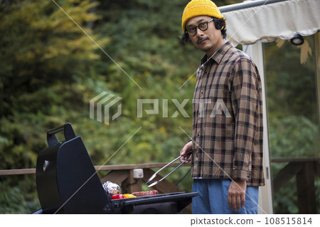 A man grilling food on a barbecue stove at a glamping facility 108515814