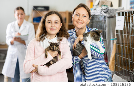 Preteen girl with mother standing in animal shelter holding cats 108516186