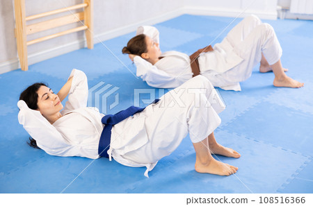 Two women in kimono doing abdominal exercises in gym Two women in kimono doing abdominal exercises in gym 108516366