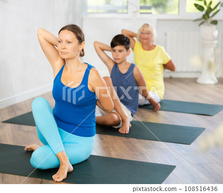 Middle-aged woman practicing cow face pose of yoga in light fitness room Middle-aged woman practicing cow face pose of yoga in light fitness room 108516436