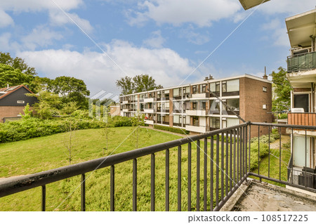 an apartment complex with green grass and trees in the foreground area on a sunny day, taken from a balcony an apartment complex with green grass and trees in the foreground area on a sunny day, taken from a balcony 108517225