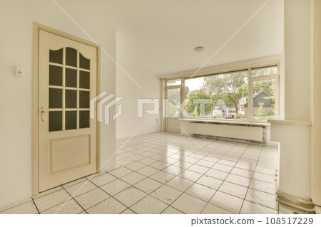 an empty room with white tile flooring and large windows looking out onto the street in front of the house an empty room with white tile flooring and large windows looking out onto the street in front of the house 108517229