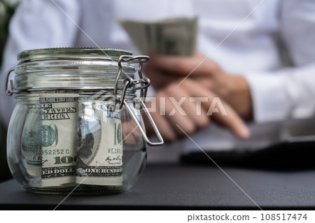 Dollar Banknote Saving Money In Glass Jar. Unrecognizable man calculate money on calculator Moderate Consumption And Economy Collecting Money Tips Business Finance 108517474