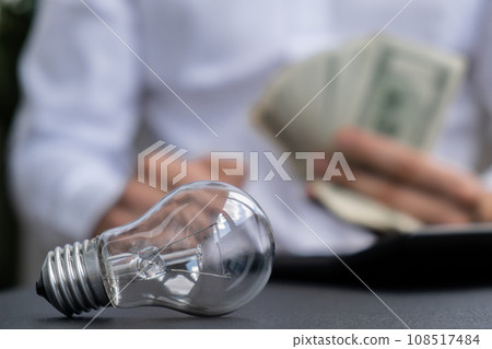 Electric light bulb. Man hands counting expenses on electricity banknotes of dollar cash accounting on calculator. Close up of hands unrecognizable Businessman. High prices for energy. Save up budget 108517484