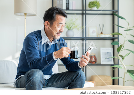 Middle-aged man looking at smartphone while drinking coffee Middle-aged man looking at smartphone while drinking coffee 108517592