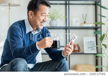 Middle-aged man looking at smartphone while drinking coffee Middle-aged man looking at smartphone while drinking coffee 108517593
