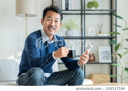 Middle-aged man looking at smartphone while drinking coffee Middle-aged man looking at smartphone while drinking coffee 108517594