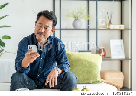 A senior man uses a smartphone in the living room. A senior man uses a smartphone in the living room. 108518154