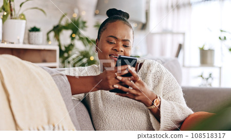Black woman, relax and typing on smartphone on sofa, reading social media post and contact chat at home. Mobile, app and download digital games, scroll technology or multimedia notification in lounge Black woman, relax and typing on smartphone on sofa, reading social media post and contact chat at home. Mobile, app and download digital games, scroll technology or multimedia notification in lounge 108518317