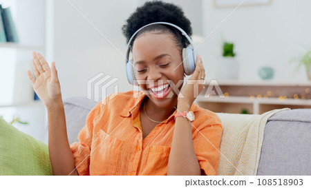 Dance, headphones or happy black woman on sofa for music streaming, mental health or wellness. Energy, couch or fun African person listening to audio technology and singing a hip hop song to relax 108518903