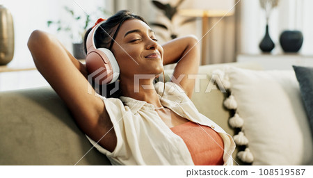 Woman, headphones and relax with music, sofa and peace with sound, smile or hearing in home living room. Girl, listening and audio streaming subscription on lounge couch, happy or radio show in house 108519587