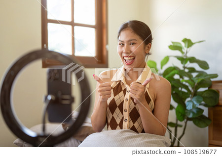 A beautiful Asian female influencer is showing thumbs up to the camera, recording her video. A beautiful Asian female influencer is showing thumbs up to the camera, recording her video. 108519677