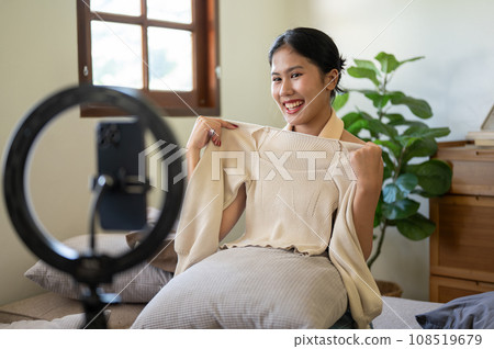 A beautiful female influencer or online seller is showing and reviewing her clothes to the camera. A beautiful female influencer or online seller is showing and reviewing her clothes to the camera. 108519679