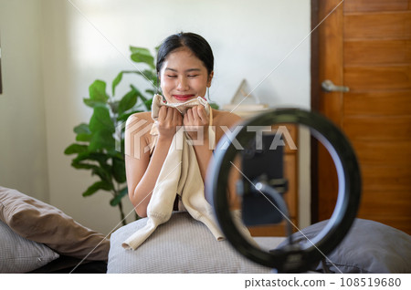 A charming female influencer or online seller is showing and reviewing her clothes to the camera. A charming female influencer or online seller is showing and reviewing her clothes to the camera. 108519680